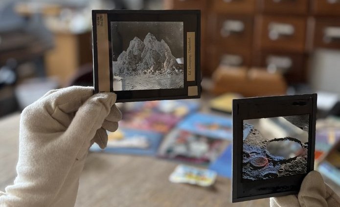 Zdjęcie przedstawia zabałaganione wnętrze i dłonie w rękawiczkach trzymające stare negatywy