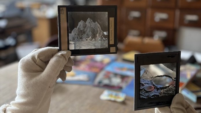 Zdjęcie przedstawia zabałaganione wnętrze i dłonie w rękawiczkach trzymające stare negatywy
