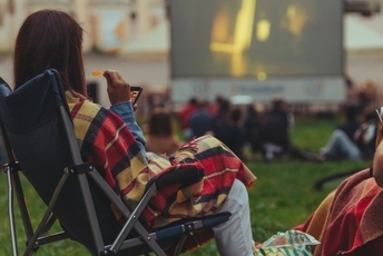 Kobieta siedzi na leżakach i ogląda film kin plenerowego
